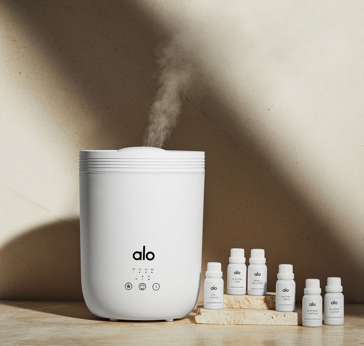 Alo’s Essential Oils and Aura Diffuser displayed upon natural rock against a tan wall. 